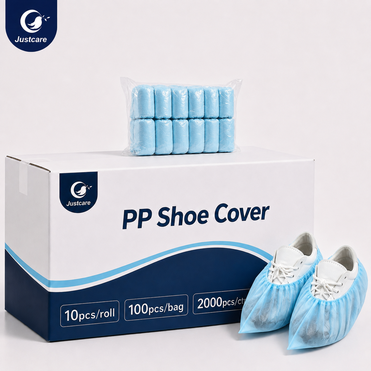 Justcare disposable PP shoe cover packaging display — a white carton box printed with the Justcare "PP Shoe Cover" logo, holding rolled blue shoe covers in transparent bags, beside a pair of white shoes wearing the blue shoe covers; pack sizes 10pcs/roll, 100pcs/bag and 2000pcs/ctn.